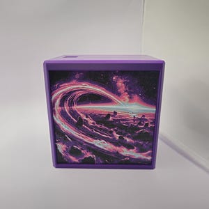 May include: A square purple box featuring a front panel with a vibrant space-themed graphic. The image displays a swirling cosmic ring, glowing pink and blue nebulae, and a dark, rocky planetary surface under a bright, distant horizon line.