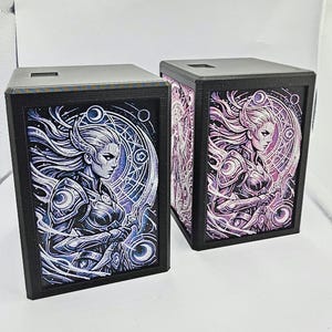 May include: Two rectangular black storage boxes featuring detailed illustrations of a warrior figure. The left box displays a blue-toned graphic, while the right box features a purple-toned graphic. Both show a character in armor with flowing hair.