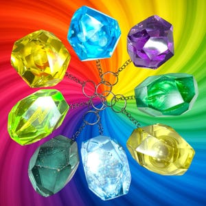 May include: A collection of eight faceted gemstone keychains in various colors, including yellow, blue, purple, green, and teal. Each gem is attached to a silver chain and ring, set against a rainbow background.