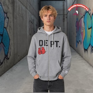 May include: A gray zip-up hoodie with the word "DEPT." printed in black and a pair of red boxing gloves. The hoodie has a drawstring hood and a white inner layer. The model is wearing black jeans.
