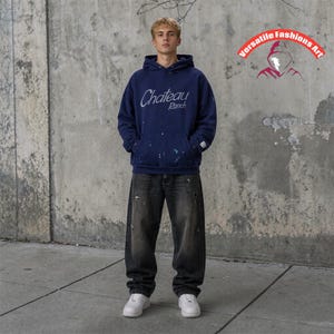 May include: A navy blue hoodie with the text "Chateau Ranch" in a cursive font, paired with black denim jeans and white sneakers. The hoodie has paint splatter details. The image also includes a logo that says "Versatile Fashions Art".