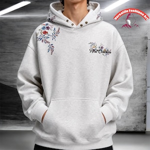 May include: A light gray hoodie with a floral design on the shoulder and hood. The hoodie has a front pocket and the text "Paul Castillan" in script. The hoodie has a drawstring hood and is made of a soft material.