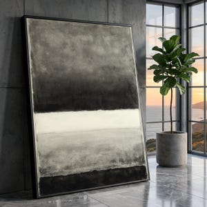 May include: Abstract framed art print with a minimalist design. The artwork features a gradient of grey and black tones with a horizontal white band. The piece is displayed in a modern interior setting with a potted plant.