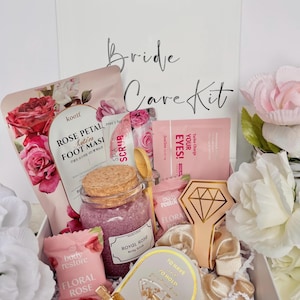 May include: A white box labeled "Bride Care Kit" filled with beauty products. Items include a rose petal foot mask, body scrub, eye patches, and floral rose products. Decorative flowers and a diamond-shaped item are also included.