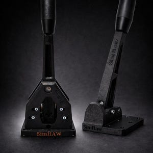 Puede incluir: Dos palancas de cambio negras para simulación de carreras con los textos "SimHAW" y "Shifter V2" visibles. Las palancas tienen una base, un soporte vertical y un mango. El fondo es oscuro.