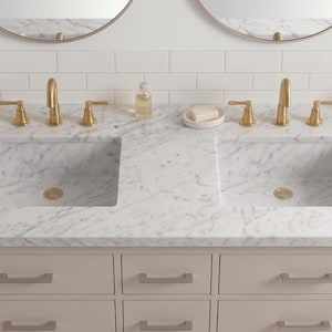 May include: A double vanity cabinet featuring a white marble countertop with gray veining and two rectangular undermount sinks. The unit includes six drawers with silver-toned hardware and two sets of gold-toned faucets and matching drains.