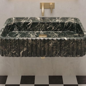 Puede incluir: Un lavabo rectangular montado en la pared, hecho de mármol verde oscuro con vetas blancas prominentes. El exterior presenta una textura estriada vertical. Un grifo de oro cepillado con un mando a juego está montado en la pared sobre el lavabo.