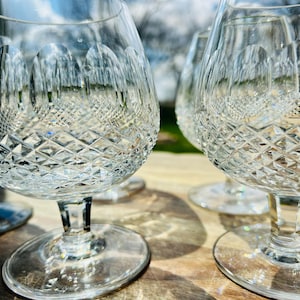 May include: Close-up of several clear crystal brandy snifters. The glasses have a diamond-cut pattern on the bowl and a rounded base. The stems are short and the glasses are on a wooden surface.