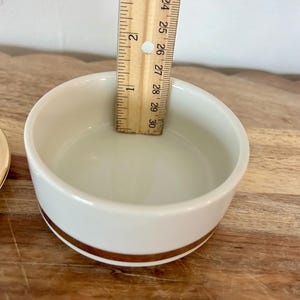 K&ouml;nnte beinhalten: Eine wei&szlig;e Keramikschale mit einem goldenen Band um den &auml;u&szlig;eren Boden. Ein Holzlineal liegt in der Schale und zeigt eine Tiefe von etwa 3,8 cm an. Die Schale hat eine glatte, gl&auml;nzende Oberfl&auml;che und ein schlichtes Design.