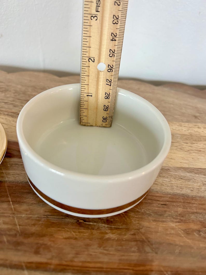 K&ouml;nnte beinhalten: Eine wei&szlig;e Keramikschale mit einem goldenen Band um den &auml;u&szlig;eren Boden. Ein Holzlineal liegt in der Schale und zeigt eine Tiefe von etwa 3,8 cm an. Die Schale hat eine glatte, gl&auml;nzende Oberfl&auml;che und ein schlichtes Design.