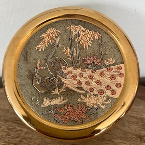 K&ouml;nnte beinhalten: Runde, goldfarbene Zierschale mit detailliertem Pfau- und Blumendesign. Die Mitte zeigt zwei Pfauen, Bambus und Blumen in Braun-, Orange- und Wei&szlig;t&ouml;nen auf gr&uuml;nem Hintergrund.