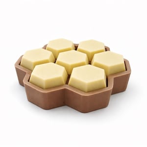 May include: A brown, honeycomb-shaped container holding seven light yellow, hexagonal-shaped objects. The container is made of a dark brown material and sits on a white surface. The objects appear to be food items.