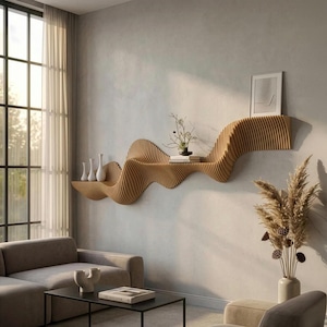 Op de afbeelding: Een modern, golvend houten wandrek met een natuurlijke afwerking. Het rek is bevestigd aan een lichtgrijze muur en bevat witte vazen, boeken en decoratieve planten. Het ontwerp voegt een unieke, artistieke touch toe aan de woonkamer.