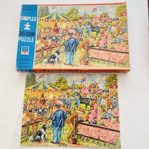 May include: A Simplex jigsaw puzzle featuring a colorful illustration of a fairground scene with people, animals, and tents. The puzzle box is visible, with the words "SIMPLEX JIG-SAW PUZZLE" printed on it. The puzzle is made in Holland.