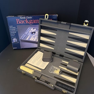 May include: A Family Classics backgammon set featuring a gray padded carrying case with a woven cloth playing field, cream and black triangular points, matching checkers, two dice cups, dice, a doubling cube, and an instruction booklet.
