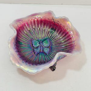 May include: Iridescent glass bowl with a butterfly design. The bowl features a ruffled edge and a vibrant color scheme of pink, purple, and green. The butterfly is centered in the bowl, and the glass has a textured, ribbed pattern.
