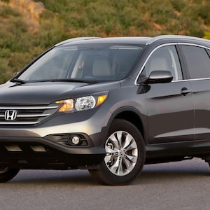 Può includere: Un SUV Honda CR-V grigio scuro con cerchi in lega argentati. Il veicolo ha una griglia anteriore con il logo Honda ed è parcheggiato su una strada asfaltata. Lo sfondo presenta un fogliame verde.