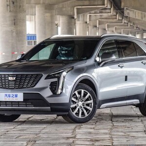 Puede incluir: Un SUV Cadillac plateado estacionado bajo una estructura de hormigón. El vehículo tiene una parrilla delantera distintiva, molduras negras y llantas de radios múltiples. El texto "汽车之家" es visible en la placa delantera.