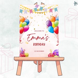 Op de afbeelding: Een verjaardagsbord op een houten ezel. De tekst luidt "Welcome to Emma's Birthday" met kleurrijke ballonnen en confetti. De datum "22 december" is ook weergegeven. Versierd met cadeaudozen en bloemen.