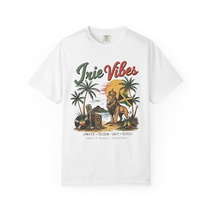 Può includere: T-shirt bianca con grafica colorata raffigurante un leone incoronato, palme e la bandiera giamaicana. Il testo include "Irie Vibes", "Jamaica, Freedom, Unity, Respect" e "Roots, Reggae, Rastafari".