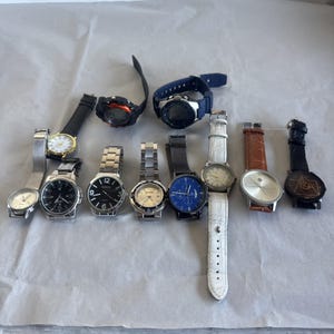 Könnte beinhalten: Eine Sammlung von zehn Armbanduhren mit verschiedenen Designs, darunter analoge und digitale Anzeigen. Die Uhren haben unterschiedliche Armbänder aus Metall, Leder und Gummi in Farben wie Schwarz, Weiß, Silber, Blau und Braun.