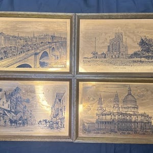 May include: A set of four rectangular wall plaques featuring detailed black and white etched illustrations of London landmarks, including London Bridge, Guildford Cathedral, a historic street scene, and St. Paul's Cathedral, all encased in wooden frames.
