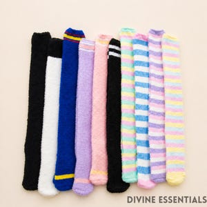 May include: A collection of knee-high fuzzy socks in various colors, including black, white, blue, purple, pink, and striped patterns. The socks have a soft, plush texture and are arranged vertically. The text "DIVINE ESSENTIALS" is at the bottom.