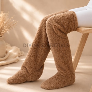 May include: Brown, fluffy, over-the-knee socks. The socks are made of a soft, plush material, appearing warm and comfortable. The socks are shown on a person sitting on a wooden chair.