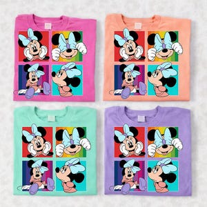 May include: Four colorful t-shirts featuring a Minnie Mouse graphic. Each shirt has a different background color: pink, peach, mint green, and lavender. The graphic is a grid of four images of Minnie Mouse with a blue bow.