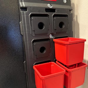 Può includere: Una piastra di montaggio nera Milwaukee PACKOUT con quattro slot di stoccaggio quadrati e tre contenitori di stoccaggio rossi. Il logo Milwaukee è rosso nella parte superiore della piastra. I contenitori sono impilati sul lato destro.