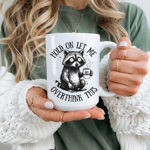 Hold On Let Me Overthink This ceramic mug — Soft Menace raccoon design — funny coffee mug — overthinking gift — raccoon meme mug — pairs with the raccoon graphic tee — Soft Menace Co