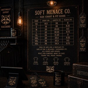 Soft Menace Co. t-shirt size chart and garment measurements displayed in dark gothic aesthetic layout with cinematic amber lighting. Includes chest width, body length, sleeve measurements, and fit recommendations for Comfort Colors 1717 graphic tees. Alternative clothing brand sizing reference card designed for gothic fashion shoppers, oversized t-shirt lovers, and punk streetwear customers.