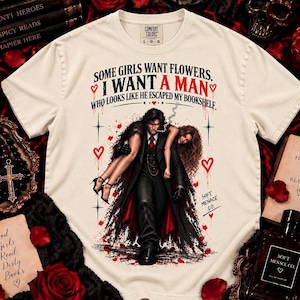 Ivory Comfort Colors 1717 bookish graphic shirt featuring dark romance artwork and “Some Girls Want Flowers, I Want a Man Who Looks Like He Escaped My Bookshelf.” Distressed black and blood red illustration of a dark-haired fictional man carrying a woman creates a gothic romance aesthetic for spicy book readers, fictional boyfriend fans, BookTok readers, morally gray men lovers, romance readers, and bookish women. Soft Menace Co. tee.