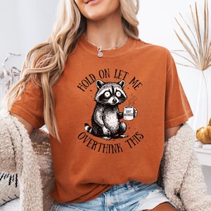 Raccoon shirt in Terracotta — Hold On Let Me Overthink This graphic tee on model — Comfort Colors 1717 warm rust colorway — funny oversized women’s shirt — raccoon meme tee — soft garment dyed