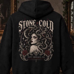 Könnte beinhalten: Ein schwarzer Kapuzenpullover mit einer Grafik auf der Rückseite. Das Design zeigt eine Frau mit Schlangen als Haaren, einen Halbmond und rote Rosen. Der Text lautet STONE COLD, SOFT MENACE CO. sowie PRETTY BUT BETRAYING in gotischer Schrift.
