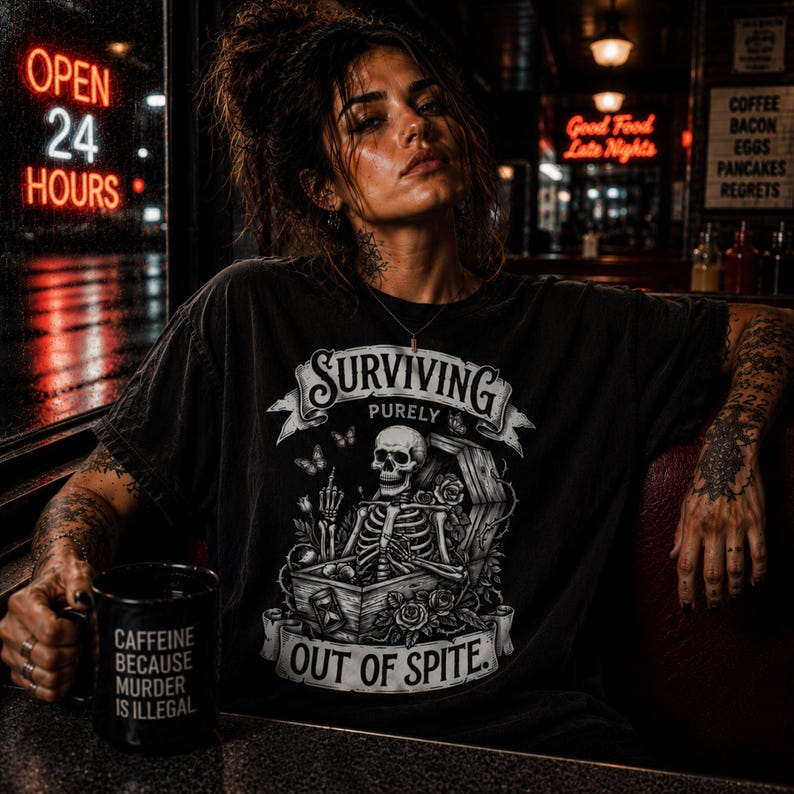 May include: Black t-shirt with a skeleton graphic in a coffin, the text reads "SURVIVING PURELY OUT OF SPITE." A black mug with the text "CAFFEINE BECAUSE MURDER IS ILLEGAL." Neon sign reads "OPEN 24 HOURS."