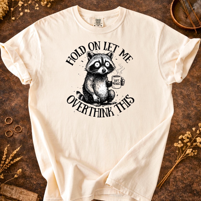 Hold On Let Me Overthink This raccoon shirt in Ivory — Comfort Colors 1717 flat lay — panic eyes raccoon graphic tee — soft garment dyed cotton — funny women’s shirt — raccoon meme shirt