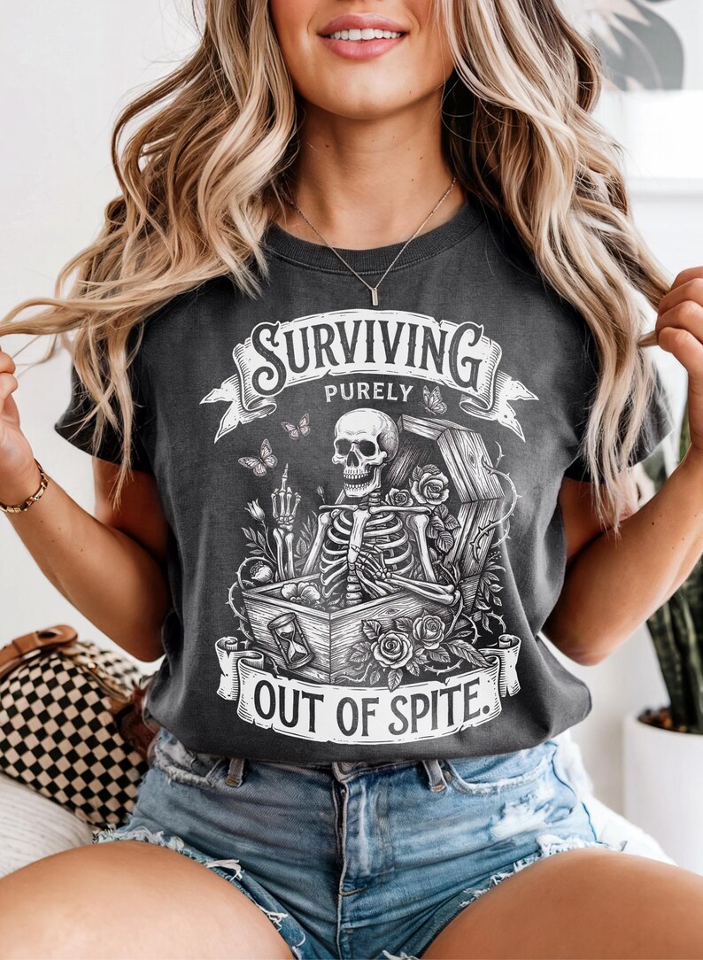 Pepper Comfort Colors skeleton shirt worn by smiling woman in casual setting. Gothic coffin illustration with roses and butterflies. Dark academia graphic tee — Surviving Purely Out Of Spite.