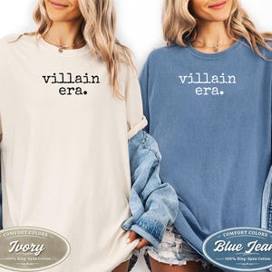 May include: Two t-shirts, one ivory and one blue jean, each with the text "villain era." printed in black and white. The ivory shirt has a Comfort Colors label that says "Ivory" and "100% Ring-Span Cotton." The blue jean shirt has a Comfort Colors label that says "Blue Jean" and "100% Ring-Spun Cotton."