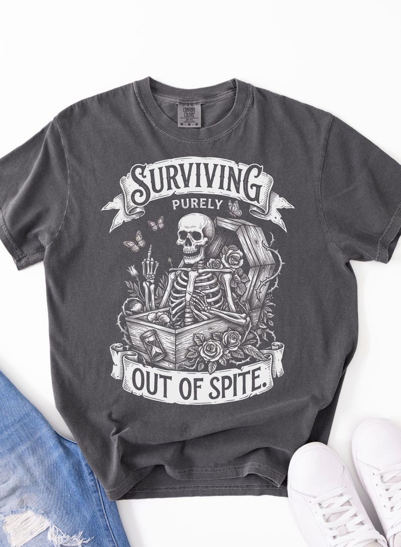 Pepper Comfort Colors 1717 skeleton shirt flat lay with jeans and white sneakers. Gothic illustration with coffin, roses, butterflies. Dark academia shirt — Surviving Purely Out Of Spite. DTG printed.