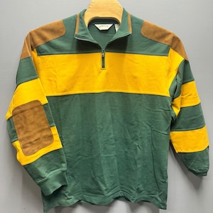May include: A green, yellow, and brown long-sleeve pullover with a quarter-zip closure. The shirt features a yellow horizontal stripe across the chest and brown patches on the shoulders and elbows. The brand name "ORVIS" is visible on the collar.