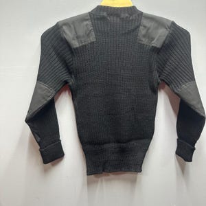 May include: A black wool sweater with reinforced shoulder and elbow patches. The sweater has a ribbed knit design and a crew neck. The patches are a darker shade of black, providing a contrast to the sweater's texture.