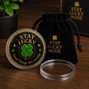 Puede incluir: Una moneda redonda en una funda protectora de plástico transparente con un trébol de cuatro hojas verde, texto dorado STAY LUCKY y Good Things Are Coming, y una bolsa de terciopelo negro con el texto dorado STAY LUCKY MODE impreso.
