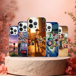 Può includere: Una collezione di custodie per telefoni con immagini colorate del film d'animazione "Toy Story". Le custodie mostrano varie scene e personaggi, tra cui Woody, Buzz Lightyear e la banda, su sfondi vivaci. Le custodie sono esposte su un piedistallo marrone chiaro.