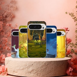 May include: A collection of five phone cases featuring vibrant illustrations from a fairytale. The cases showcase scenes with characters in a swamp, a forest, and a night sky. The cases are displayed on a round, light-colored pedestal.