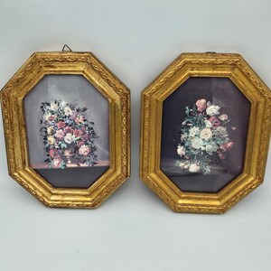 May include: Two octagonal wall frames with ornate gold-toned borders. Each frame contains a floral still life print featuring a bouquet of colorful flowers in a vase. The left print has a light gray background, while the right print has a dark background.