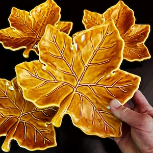 May include: A set of three glossy, golden-brown ceramic dishes shaped like maple leaves. Each dish features a detailed, embossed vein pattern across the surface, with a smooth, reflective finish that highlights the organic, pointed leaf edges.