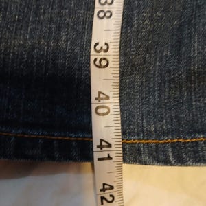 May include: A dark blue denim fabric with visible stitching, positioned next to a white measuring tape that indicates a length measurement extending past 40 inches, with the tape showing increments from 37 to 43 inches clearly displayed.