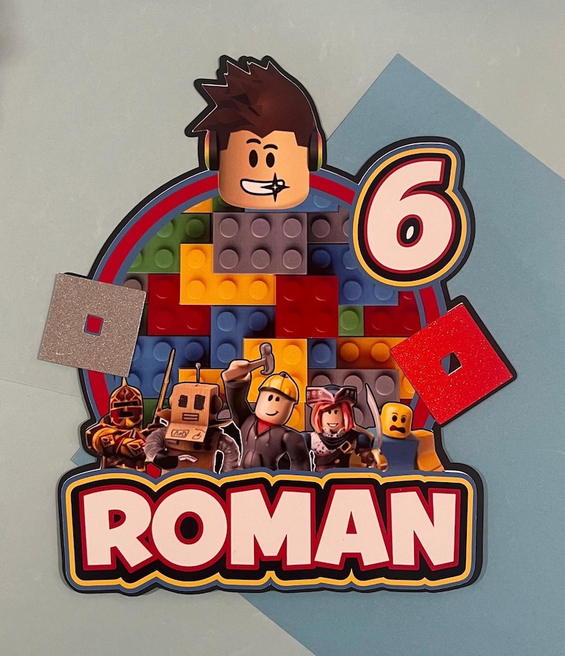 May include: A colorful birthday cake topper featuring a Roblox character design. The topper includes a large number 6, the name "ROMAN", and various Roblox figures. The background is made of colorful building blocks.