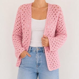 Op de afbeelding: Een lichtroze gehaakt vest met een open weefsel. De jas met lange mouwen heeft een relaxte pasvorm en een klassieke open voorkant. Het vest wordt gecombineerd met een witte tanktop en lichtblauwe jeans.